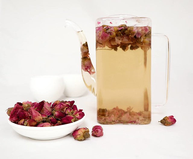 White dish of pink rosebuds beside glass pitcher of rosebud tea