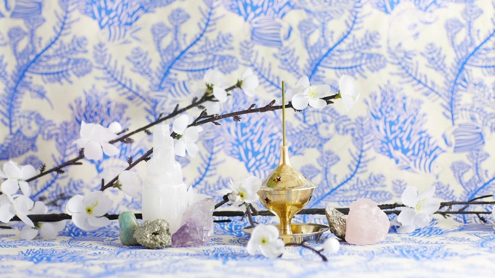 Gold incense burner with white flowers and crystals in front of blue floral paper
